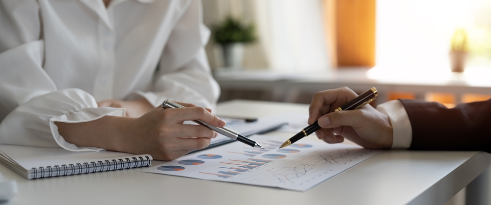Two people at a white desk reviewing printed financial charts with pens in hand during a financial planning session for a Lake Macquarie client