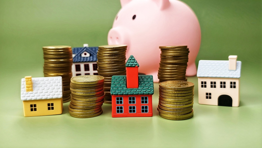 Miniature houses and stacks of gold coins arranged in front of a pink piggy bank, representing wealth planning for a Port Stephens client